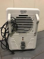 Front view of the DeLonghi electric heater showing vents, two control knobs, safety labels, and attached power cord.