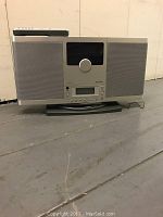 Front view of Brookstone AM/FM CD player showing speaker grills, central dial, screen and front panel controls.