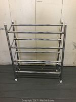 Front view of extendable metal shoe rack, showing horizontal rods and white plastic end caps on the legs and top of vertical bars.
