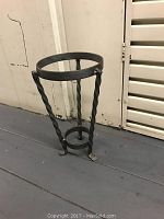 Photo of a black metal glass vase holder, shown on a floor near white shutter door, repurposed as an umbrella stand.