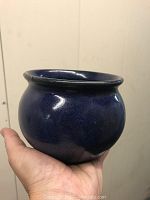 A small rounded ceramic pot in dark blue glaze held in a hand to show size and shape.