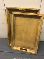 Photo showing both wooden trays leaned against the wall, smaller tray nested inside larger tray