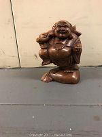Front view of carved wooden Buddha figurine showing a smiling figure holding an item, with intricate wood grain and carved details