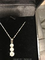 Close-up photo of diamond chip necklace with pendant showing three clear stones set vertically in silver-tone metal on a chain inside a black jewelry box.