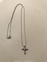 Photo showing full length of necklace with cross pendant on a plain surface.