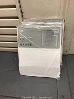 Photo of three sheer curtain packages stacked together, white fabric visible through packaging, brand 'LILL' on packaging with curtain size and care symbols.