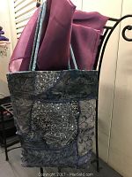 Front view of sequined cloth tote bag showing the patchwork design with sequins and embroidery in shades of blue and gray, hanging on a chair.