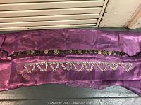 Two fashion belts laid out flat on a purple cloth background, showing details of a silver-toned belly chain belt and a wooden link string belt.