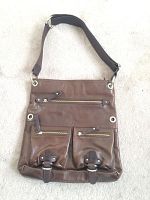 Front view of the brown leather messenger tote bag showing multiple zippered pockets and the adjustable cloth shoulder strap.