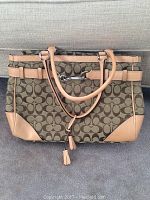 Coach handbag with signature 'C' pattern canvas and tan leather trim and handles, placed on a gray surface.