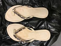 Pair of beige flip-flops with fish leather trimmed straps shown on a dark background.