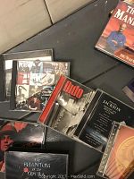 Photo of assorted music CDs and cassette tapes laid on a dark surface, featuring covers from Phantom of the Opera, Michael Jackson, Creed, and others.
