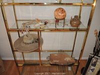 Photo of shelf displaying the Elk Dreamer dance stick, large woven jute hat, stone hanging pot, and decorative globe on tripod stand.