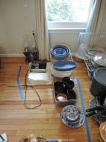 Wide shot of soup crocks, nested mixing bowls, chip and dip servers, assorted small bowls, napkins and place mats on floor.