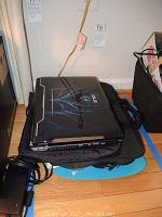 ASUS G51V laptop closed showing top lid with blue tribal graphics. Laptop rests on protective sleeves and bags.