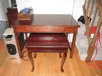 Front view of a dark wood vintage desk with a center drawer and a matching smaller side table underneath. Desk shows minor leg scratches and one missing drawer pull.