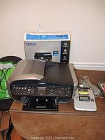 Canon MX850 printer, Brother P-Touch label maker, HP OfficeJet printer box and Epson ink cartridge on table.