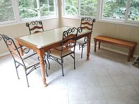 Wide shot showing the wood and tile dining table, metal and wood chairs around it, and a wooden bench alongside the set in a well-lit room with windows.