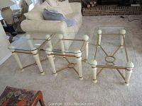Three matching tables consisting of one rectangular coffee table and two square end tables with glass tops, white wooden legs featuring spherical finials, and gold-tone metal decorative frames with a distressed finish on the legs.