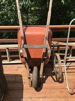 Front view of the orange metal wheelbarrow with wooden handles and rubber tire