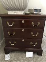 Full frontal view of mahogany nightstand showing all three drawers closed with brass handles and keyholes