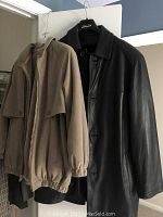Men's black leather 3/4 coat next to light brown women's jacket on hangers.
