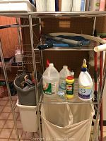 Photo showing the rolling wire laundry rack loaded with multiple cleaning bottles, a mop and broom, and bucket with brushes inside.