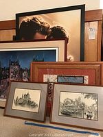 Group of six framed art pieces leaning against wall