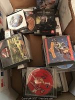 Photo showing several PC game discs and cases including The Witcher 2, Titan Quest, and Sims along with other unidentified PC games.