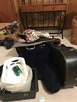 Photo showing an arrangement of various bags, a black guitar case, a black metal decorative item, and plastic containers.