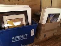 Photo showing two containers filled with various framed and mounted photographs, including a dark wooden framed photo of a yellow flower.