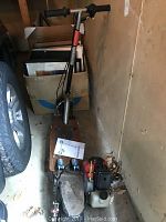 Full view of the Tornado gas scooter showing handlebar, large rear tire, and engine along with manual on top of deck.