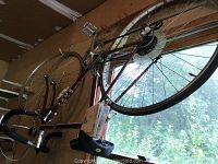 Full side view of the maroon/red Ross English racing bicycle hanging vertically indoors, showing drop handlebars, pedals, chain, and rear wheel.