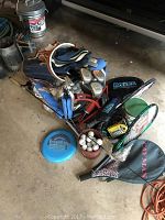 Full view of the lot including golf bag, golf clubs, golf balls, tennis rackets, fishing rod and reel, and flying disc.