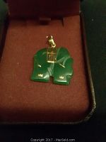 Front view of green jade pendant with gold hardware in jewelry box, showing carved details and polished surface.