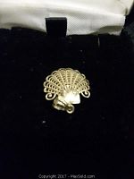 Close-up image of the 14 kt gold shell pendant placed inside a black jewelry presentation box with white interior lining, showing the detailed filigree design.