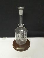 Front view of the clear blown glass bottle containing a detailed model ship, on wooden base with metal plaque.
