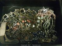 Photo showing assorted jewelry mixed in a box including chains, colorful beads and faux pearl necklaces, and several bracelets.