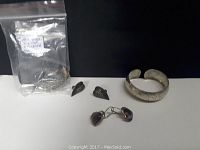 Overview photo showing all items in the jewelry lot: leaf-shaped earrings, amethyst earrings, engraved cuff bracelet, and a bag with additional items