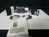 Overview of the lot showing Canon Mini DV camcorder, Nikon Coolpix camera, Canon Powershot camera, Olympus camera, software CDs, and instruction manual.
