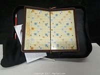 View of Scrabble game board, open inside a carrying case, showing score sheets and red pencil in the side compartment
