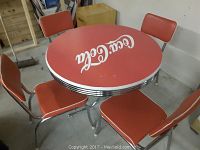 Overhead view of round red tabletop with white Coca-Cola logo and four surrounding chairs on chrome base