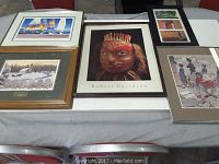 Five framed artworks laid on a table, showing variety of styles including an indigenous mask print signed Robert Davidson, winter landscape, and abstract art.