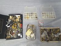 Top view showing a black box tray with assorted mixed metal-tone and beaded costume jewelry beside two plastic compartment boxes with organized small jewelry pieces.