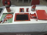 Photo showing all Coca Cola themed items arranged on table including tins, tray, chalkboard, keychain, and can.