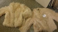Two vintage long-haired Tibetan lamb coats laid out showing their texture and condition. Coats are light beige and display signs of damage such as rips and tears.