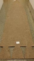Full view of the rocket shaped light brown wool felt carpet measuring approximately 13 feet long and 3 feet wide placed on a floor with some wear marks.