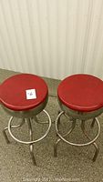 Two chrome bar stools with red vinyl upholstered round seats, shot from top and front angles, showing overall condition and seat surfaces.
