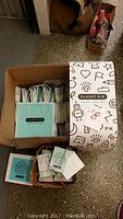 Box filled with numerous Planet Kid branded hang tags, small bags, and some packaging materials