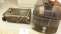 Small electric heater/fan and black humidifier side by side on floor.
